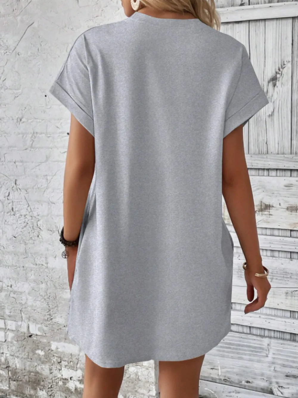 Person wearing a gray t-shirt against a textured wall.