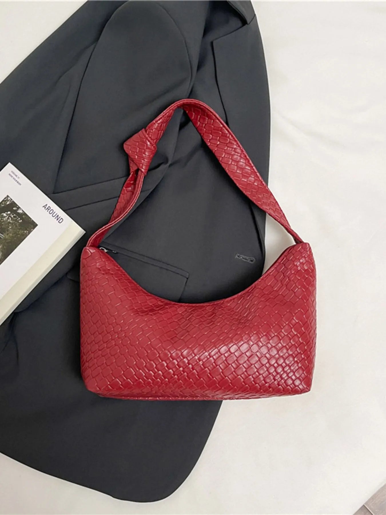 Red textured handbag on a gray suit jacket with a white surface underneath