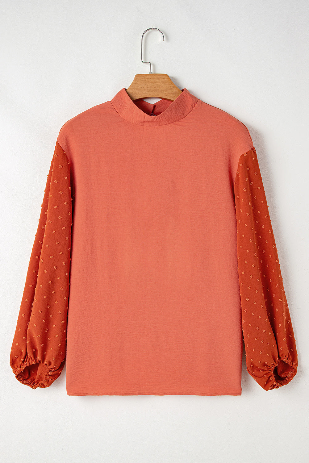 Coral-colored blouse with sheer sleeves on a wooden hanger against a white background