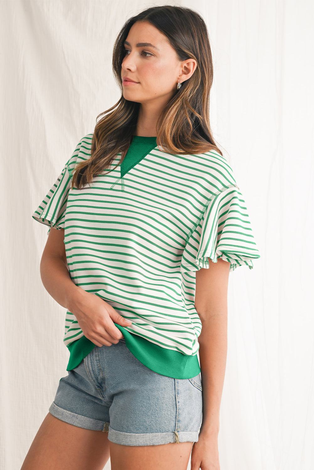 Woman wearing a green and white striped shirt with denim shorts on a plain background