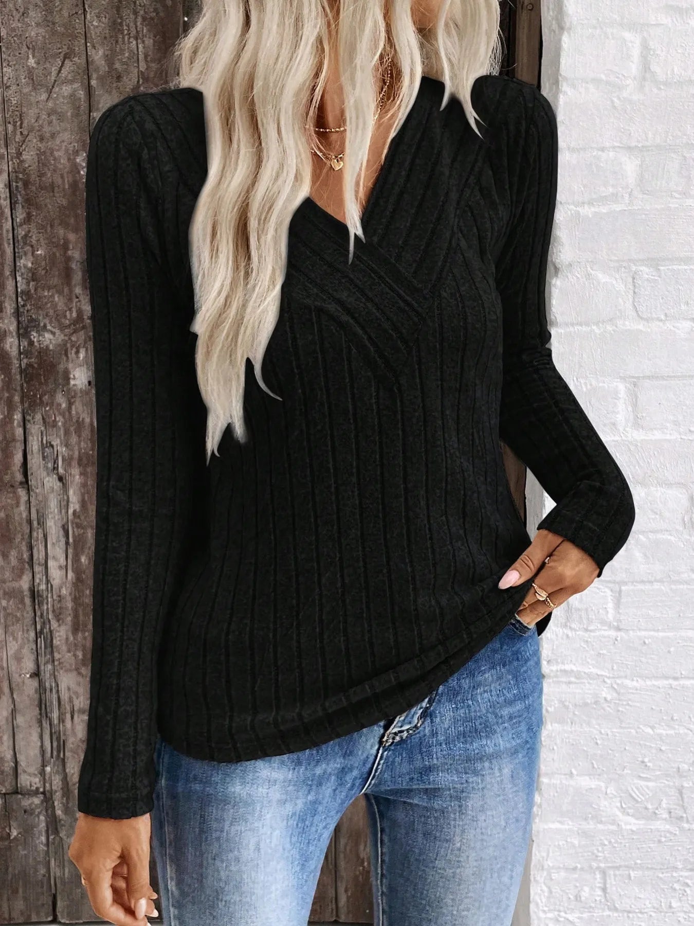 Person wearing a black ribbed sweater and blue jeans against a brick wall.