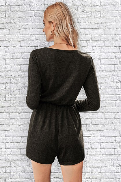 Woman wearing a black romper against a white brick wall.