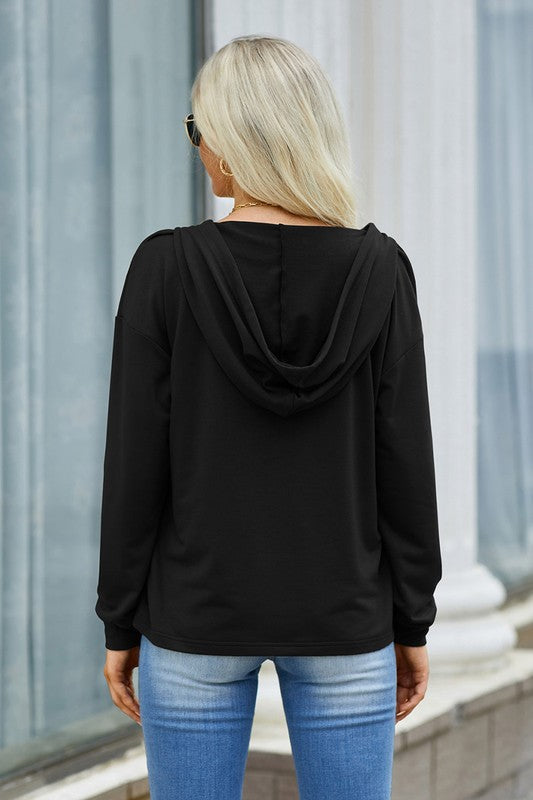 Person wearing a black hoodie and blue jeans standing against a light-colored wall.