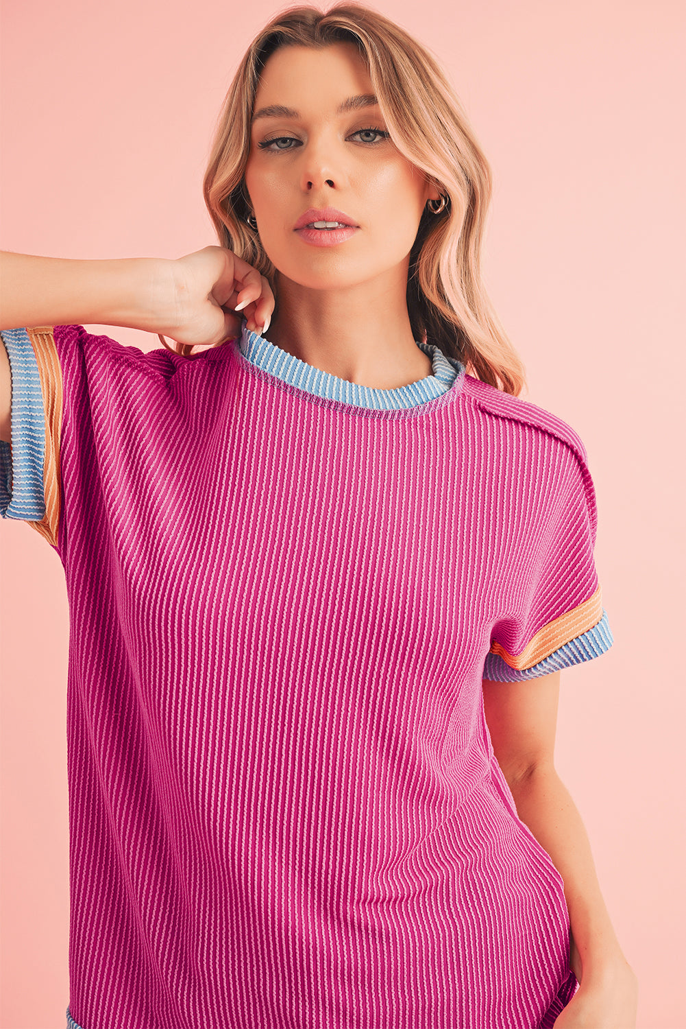 Woman wearing a pink ribbed sweater with blue trim against a pink background