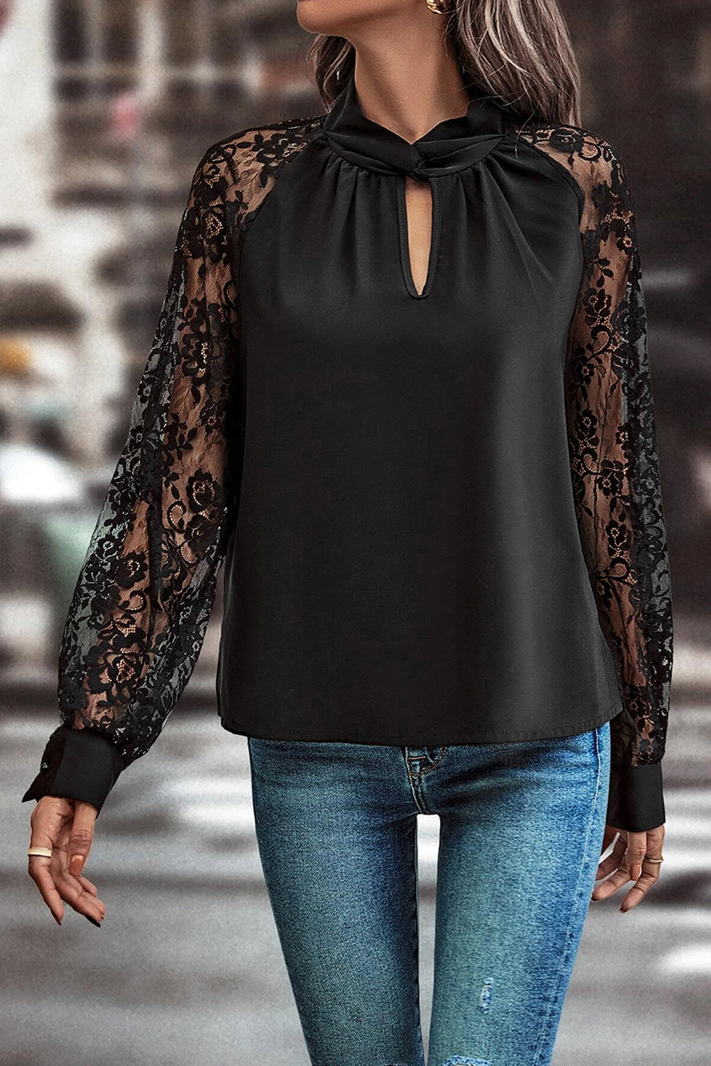 Black blouse with sheer lace sleeves worn by a person on a blurred street background