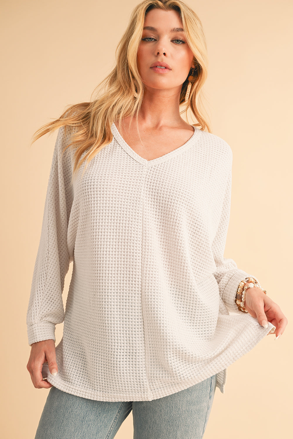 Woman wearing a beige long-sleeve textured top against a beige background