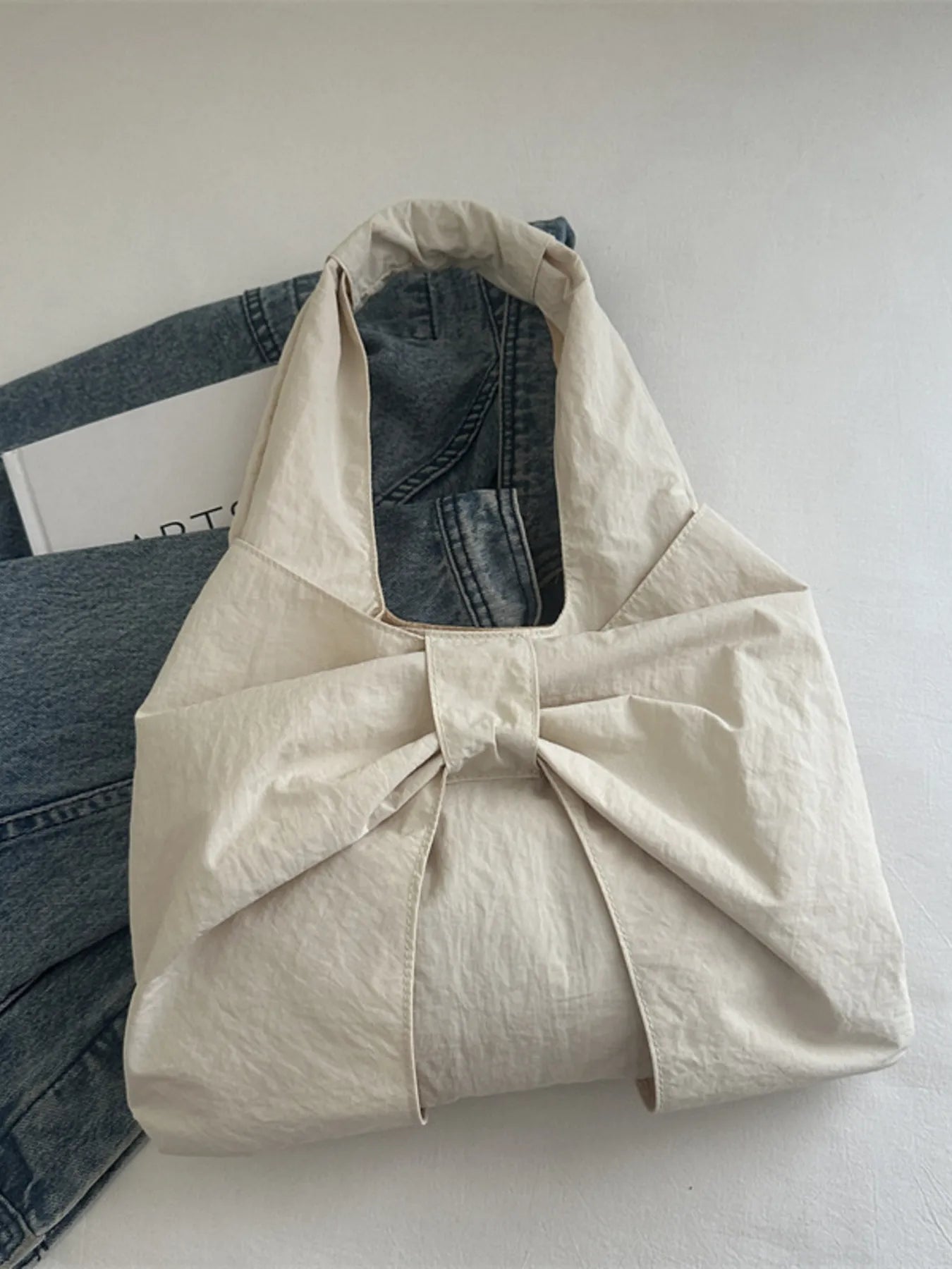 Beige tote bag with denim jeans inside on a light gray surface