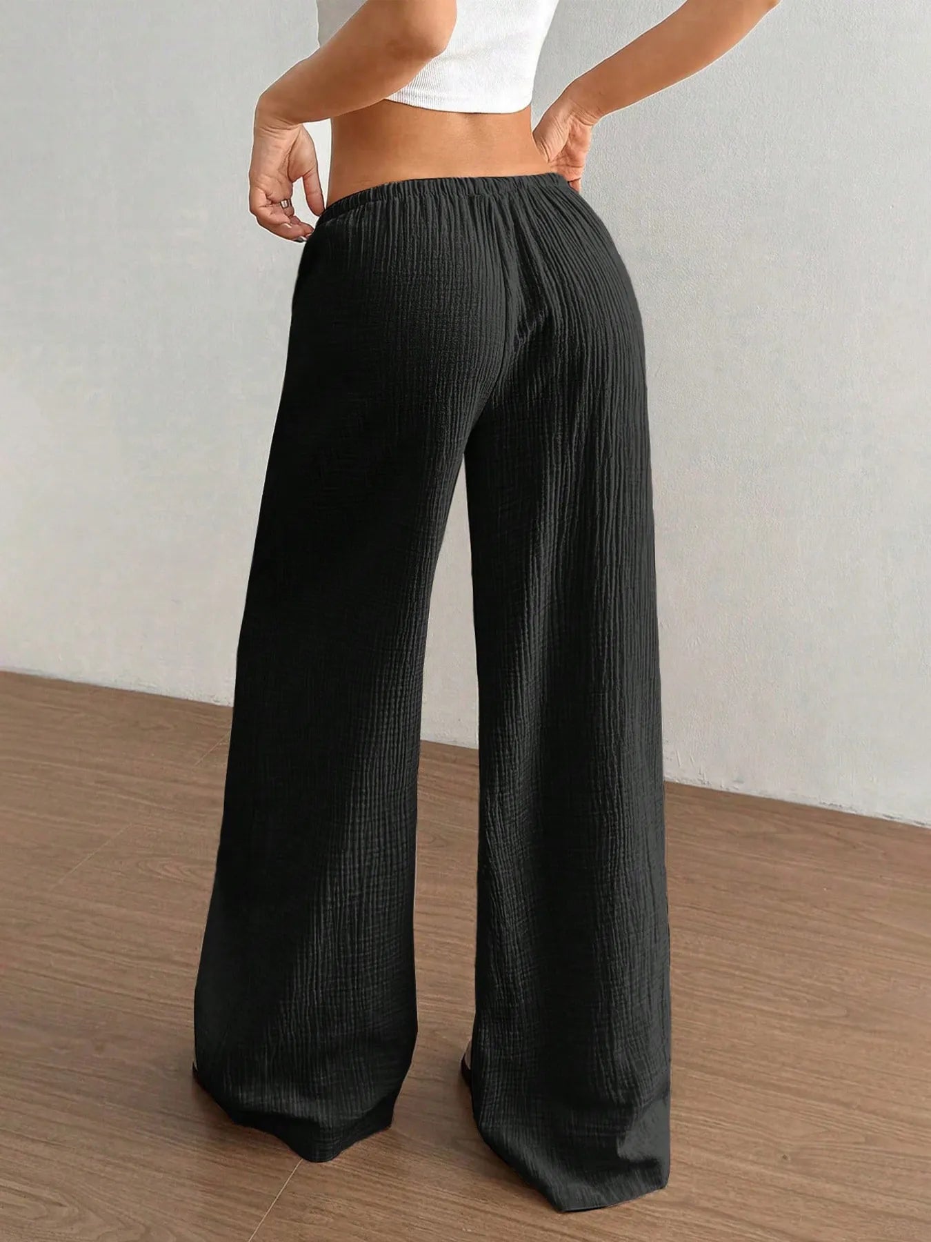 Person wearing black wide-leg pants on a wooden floor with a neutral background