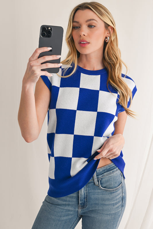 Woman wearing a blue and white checkered shirt and jeans, taking a selfie.