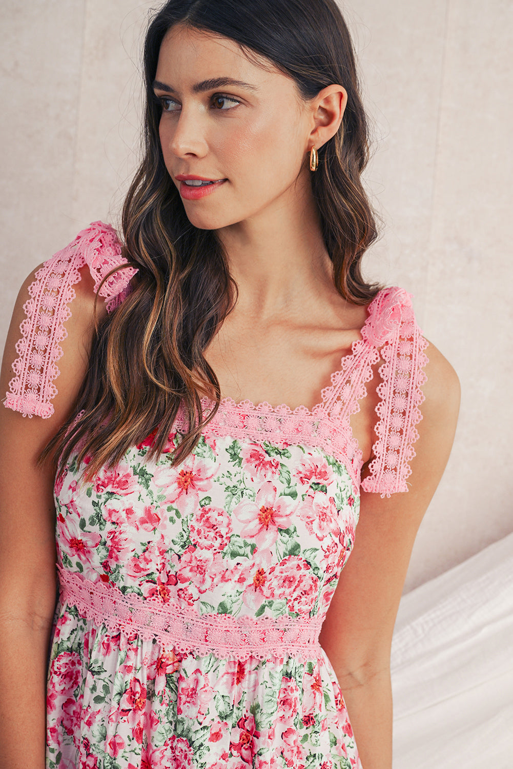 Woman wearing a floral dress with pink lace details against a neutral background
