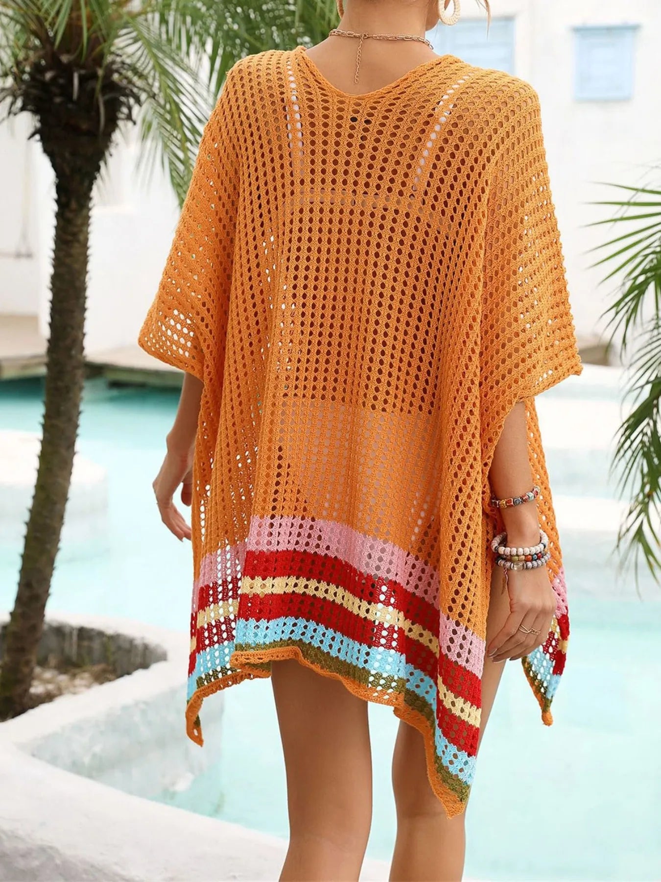 Person wearing an orange crochet cover-up with colorful hem by a poolside.