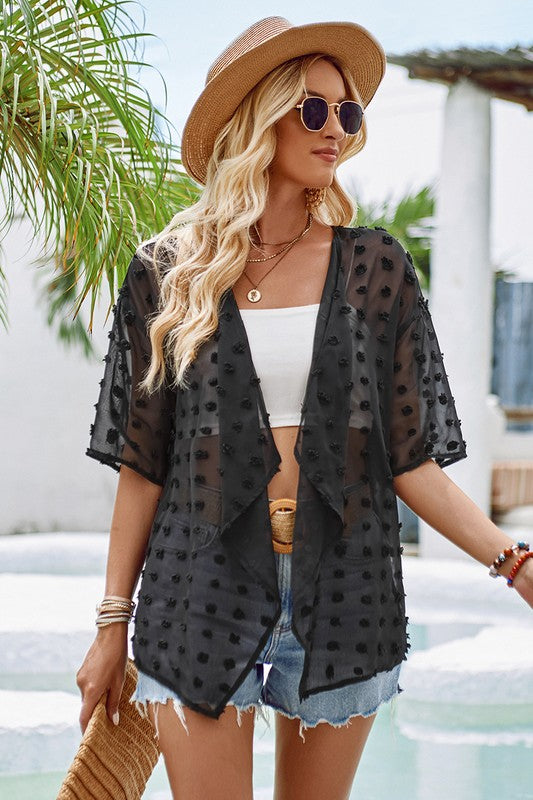 Woman wearing a black polka dot kimono, white top, denim shorts, and straw hat by a pool.