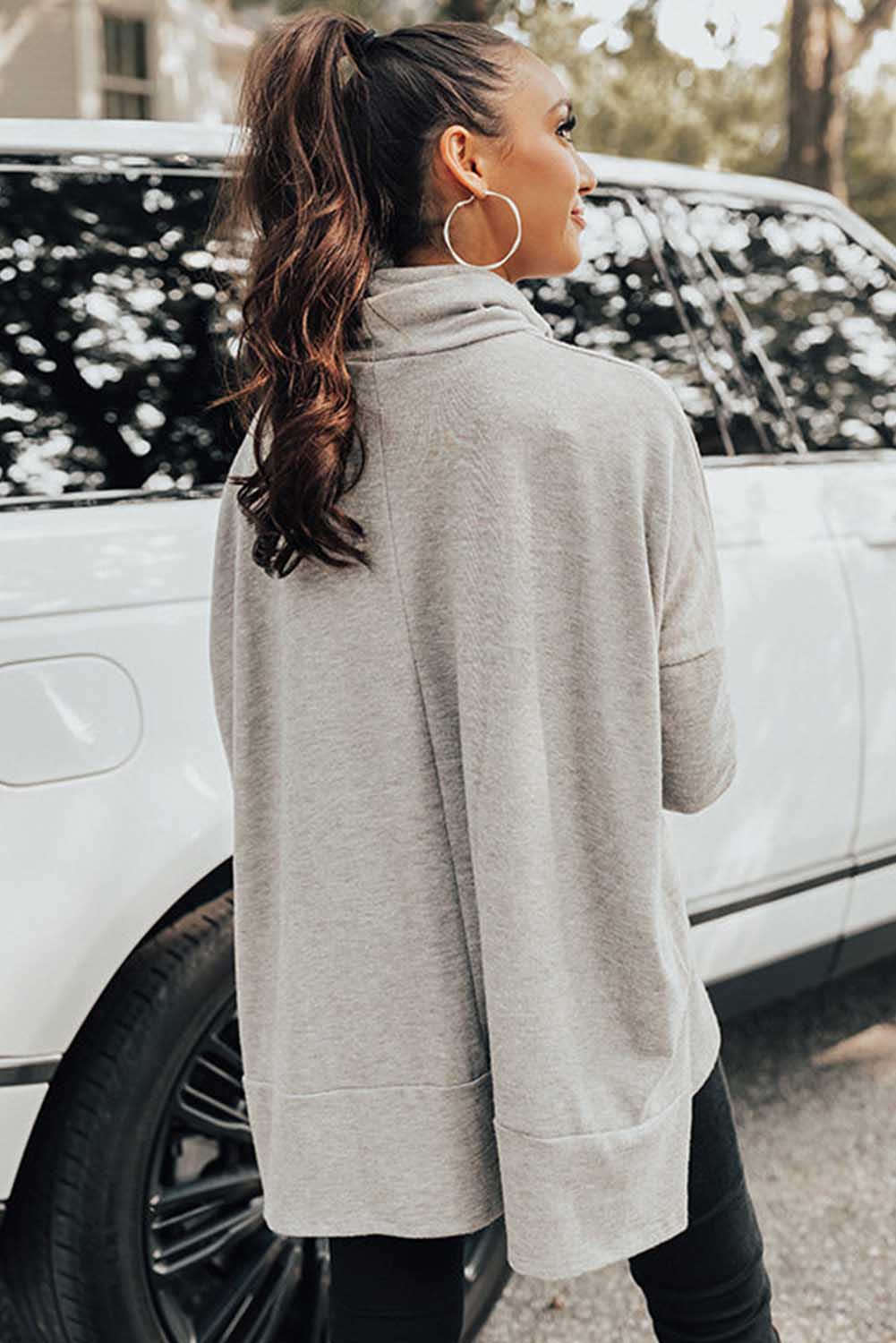 Woman wearing a light gray sweater standing next to a white car.