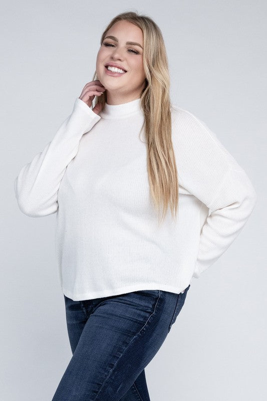 Woman wearing a white sweater and blue jeans against a plain background