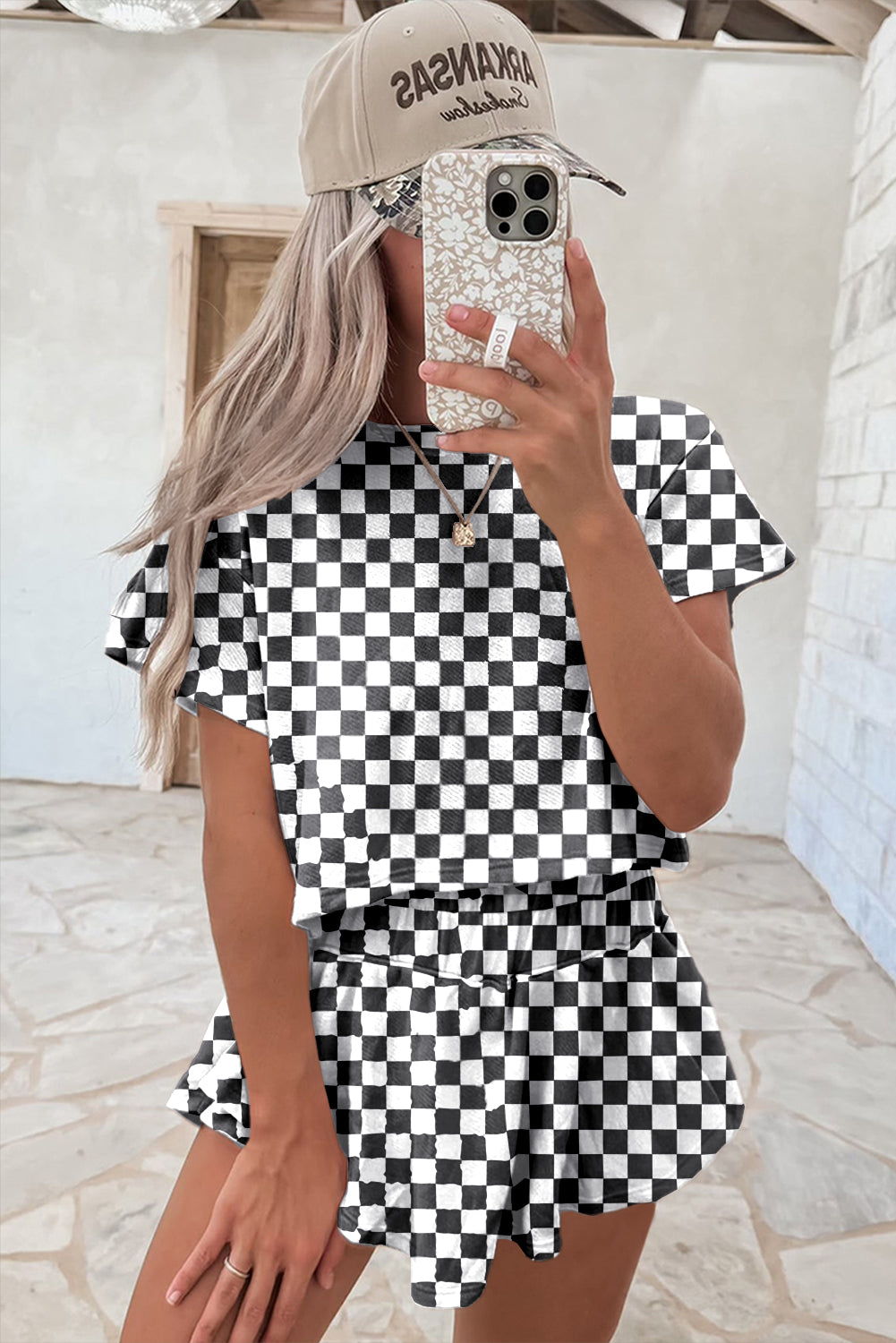Person wearing a black and white checkered dress with a beige cap and sparkling phone case.