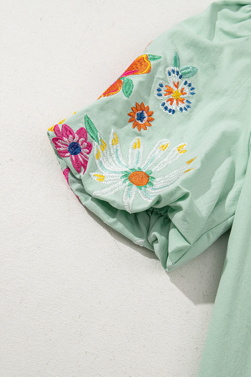 Light green fabric with colorful floral embroidery on a white background
