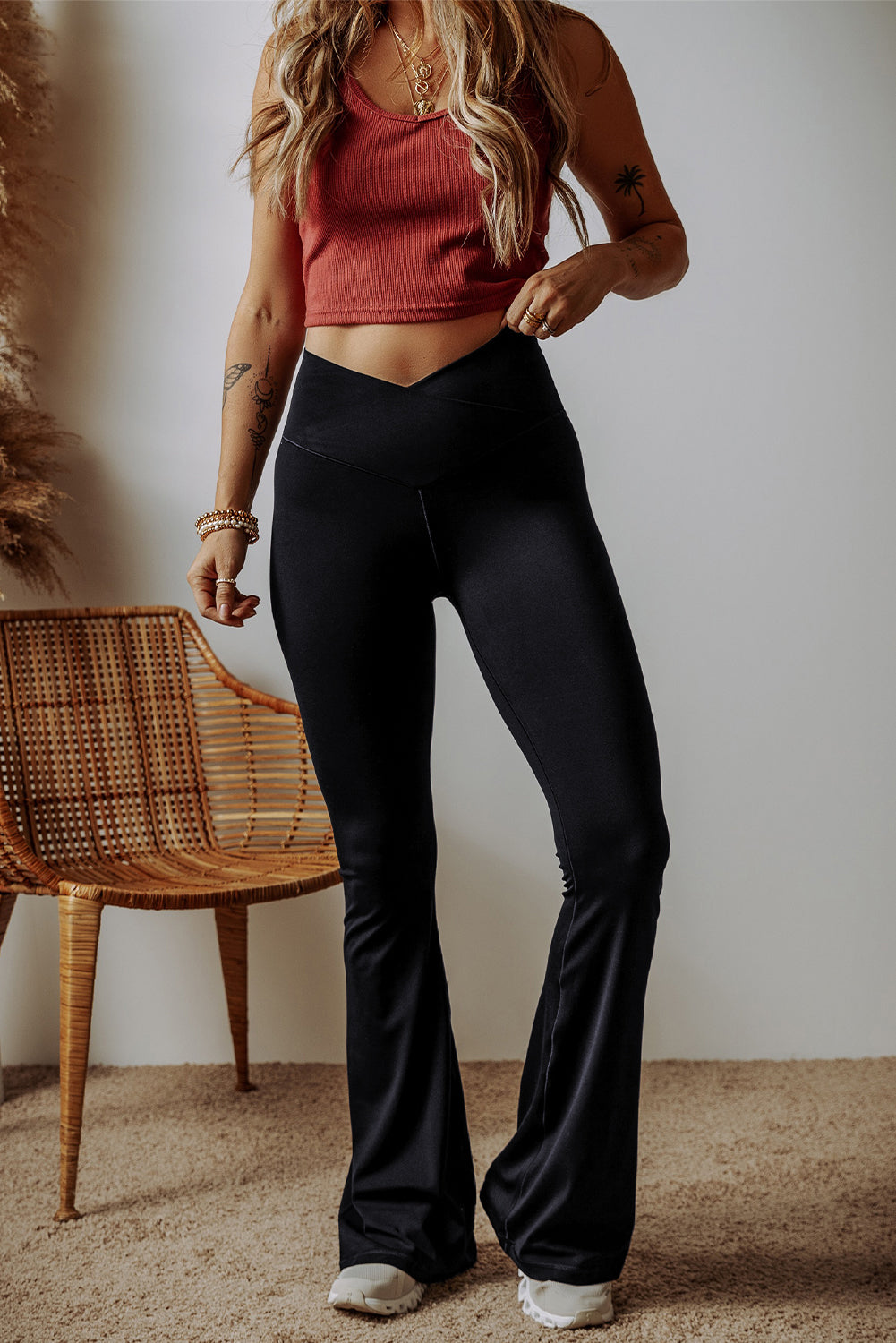 Person wearing a red crop top and black flared pants standing in a room with a wicker chair.