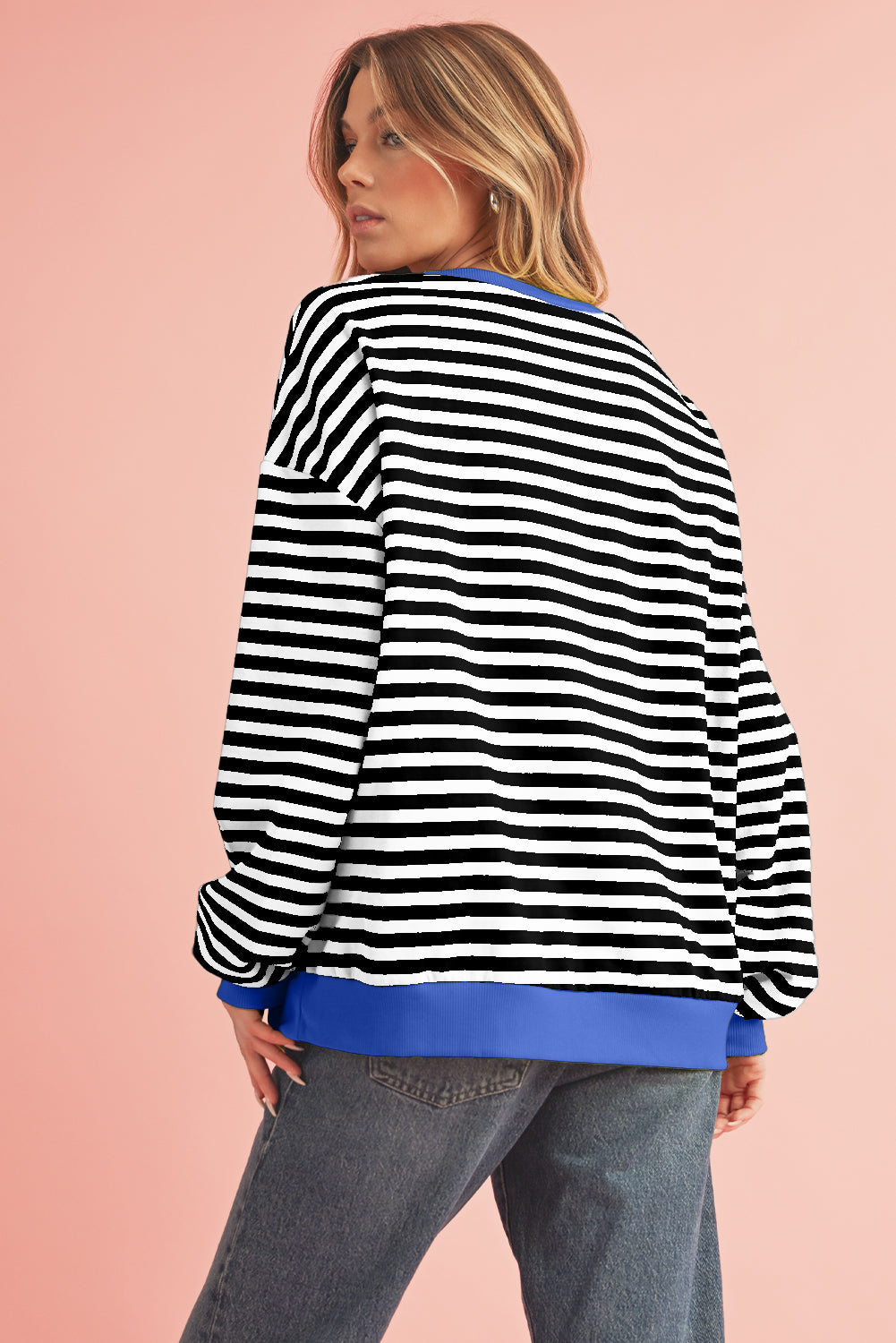 Woman wearing a black and white striped sweater with a blue trim on a pink background