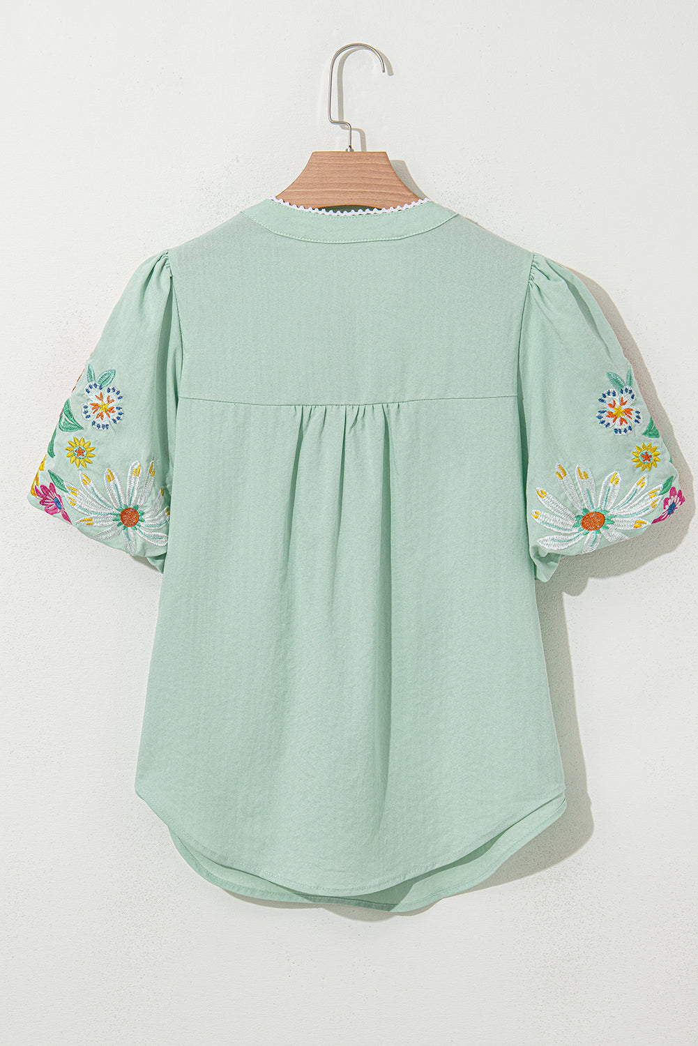 Green blouse with floral embroidery on sleeves hanging on a white background