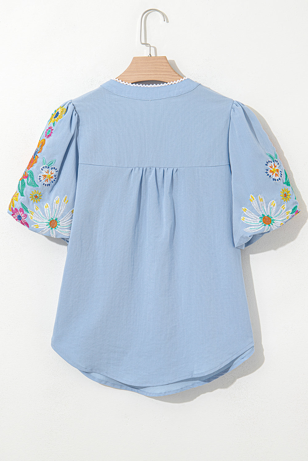 Light blue blouse with floral sleeves on a hanger against a white background