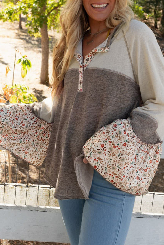 Woman wearing a two-tone sweater with floral sleeves and pockets outdoors.