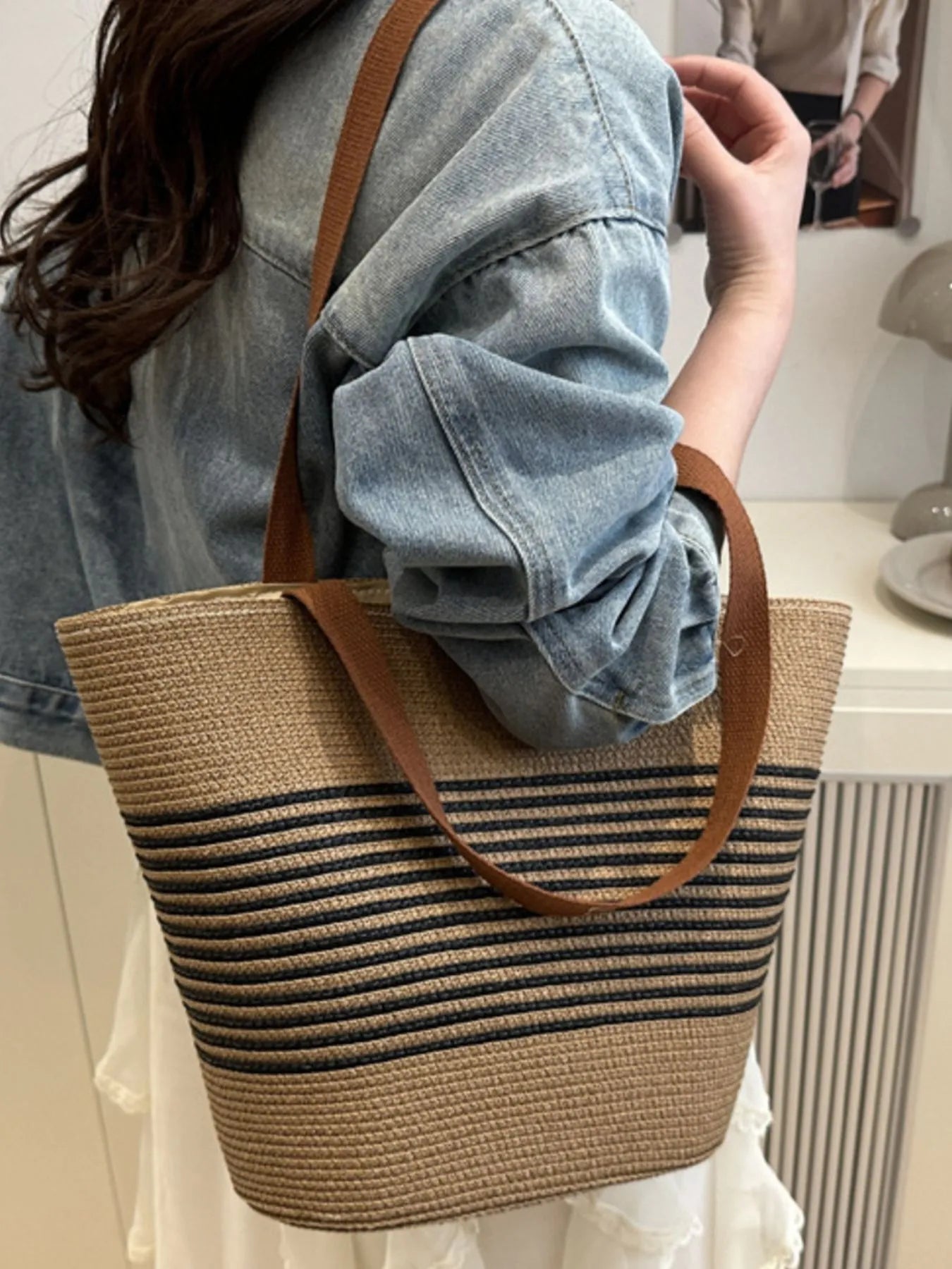 Person holding a striped straw bag with a brown strap