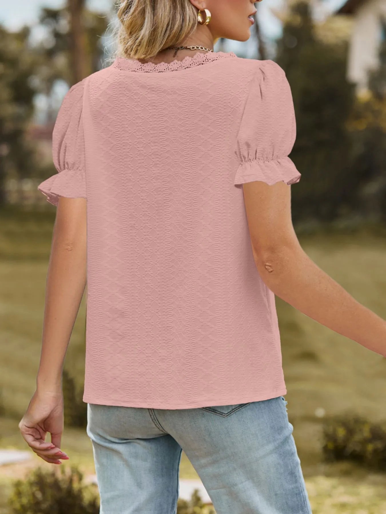 Person wearing a pink blouse with ruffled sleeves in an outdoor setting