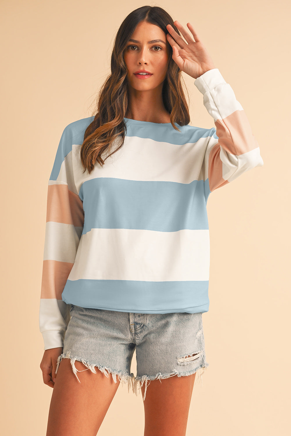 Woman wearing a striped sweater and denim shorts on a beige background