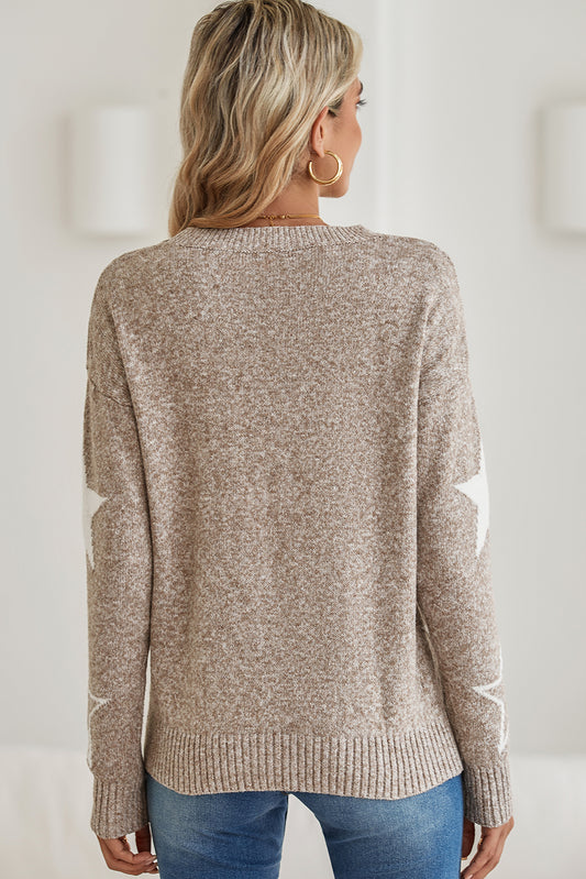 Woman wearing a beige sweater with white star patterns, holding a brown bag.