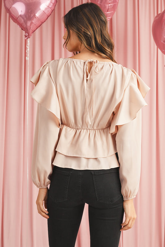 Woman wearing a light pink blouse with ruffled sleeves against a pink curtain background