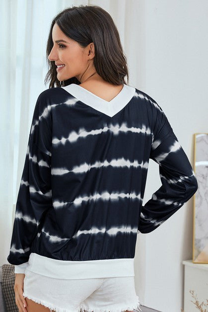 Woman wearing a navy and white tie-dye long-sleeve top in a bright room.