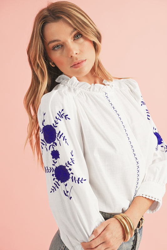 Woman wearing a white blouse with blue floral embroidery on a pink background