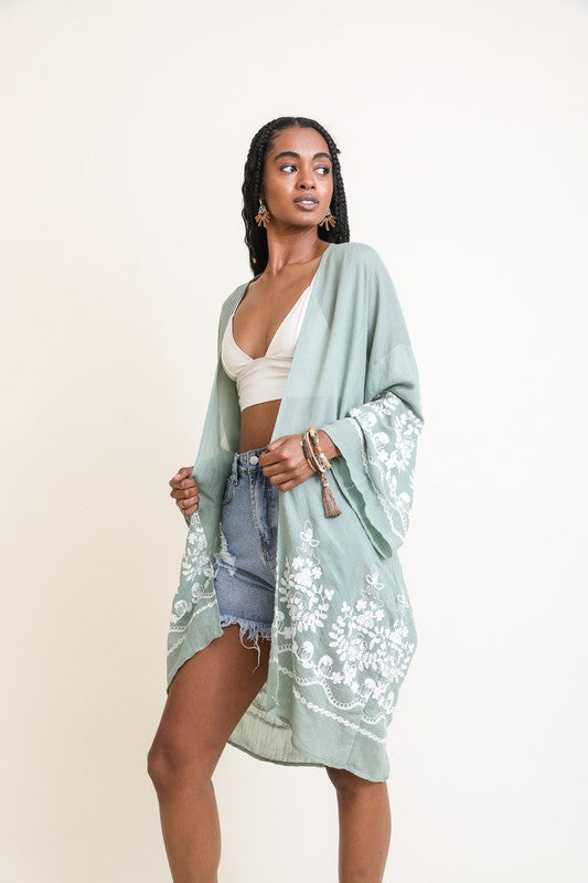 Woman wearing a light green kimono-style garment with floral patterns on a plain background