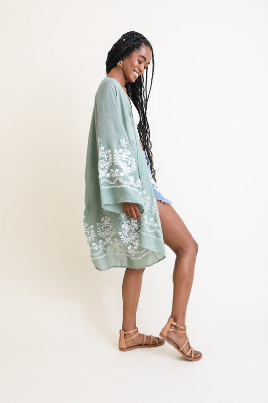 Woman wearing a light green kimono with white floral embroidery on a plain background