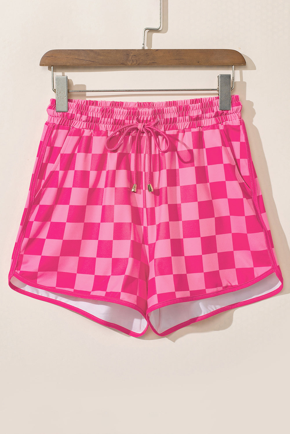 Pink checkered shorts on a hanger against a beige background