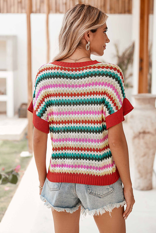 Woman wearing a colorful striped sweater and denim shorts outdoors.