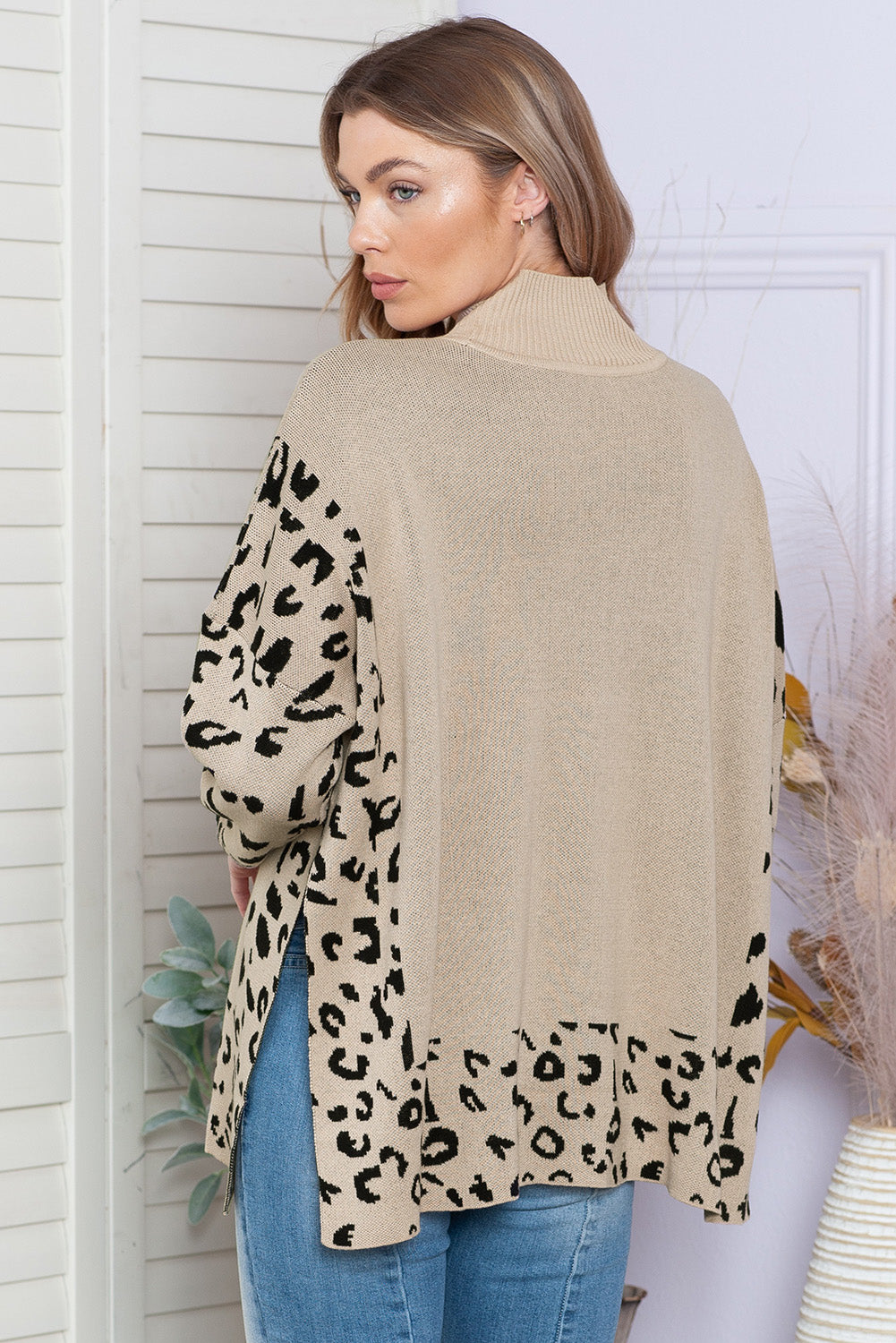 Woman wearing a beige sweater with leopard print sleeves against a white wall.