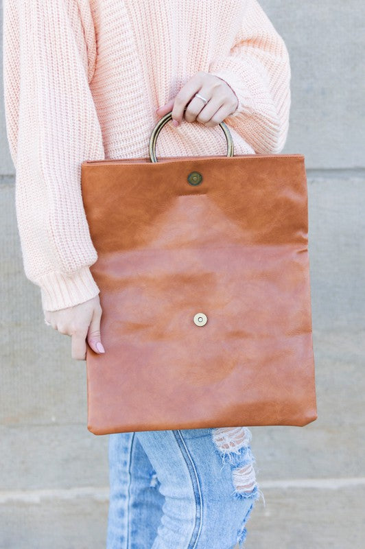 Person holding a brown leather tote bag against a neutral background