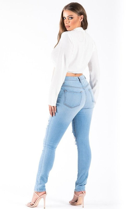 Woman wearing light blue jeans and a white cropped top on a white background