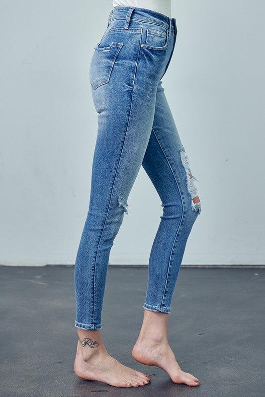 Blue jeans with distressed details worn by a person on a plain background