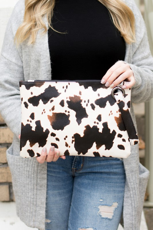 Person holding a cow print clutch bag with a neutral background