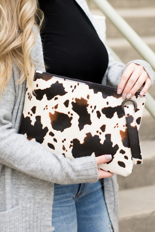 Person holding a cow print clutch bag with a neutral background