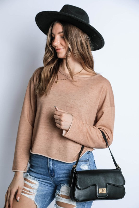 Woman wearing a beige sweater, black hat, and ripped jeans, holding a black handbag against a white background.