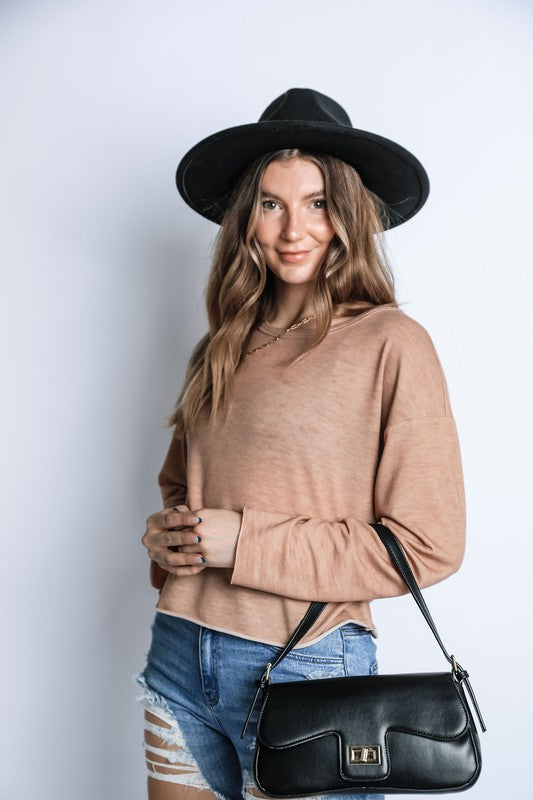 Woman wearing a beige sweater, black hat, and blue shorts with a black handbag against a white background