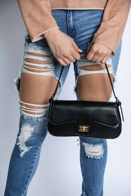 Person wearing ripped jeans and holding a black handbag against a neutral background