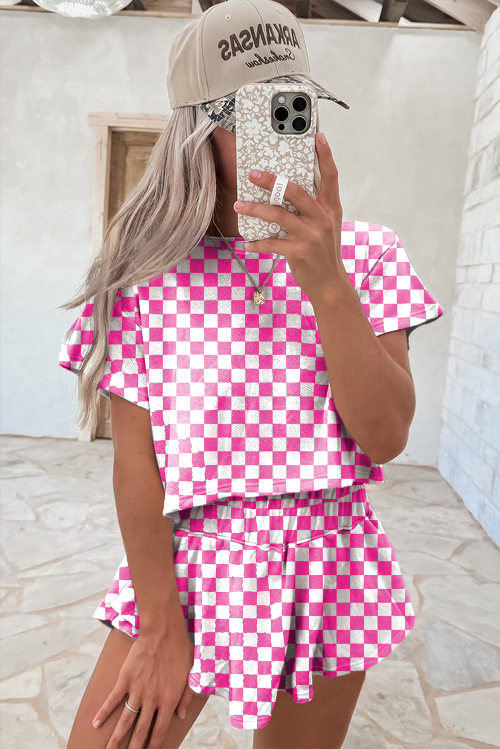Person wearing a pink and white checkered outfit with a cap and phone case.