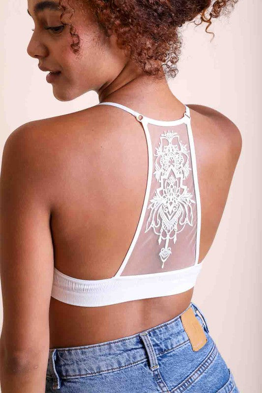 Person wearing a white lace-trimmed bralette with blue jeans on a plain background