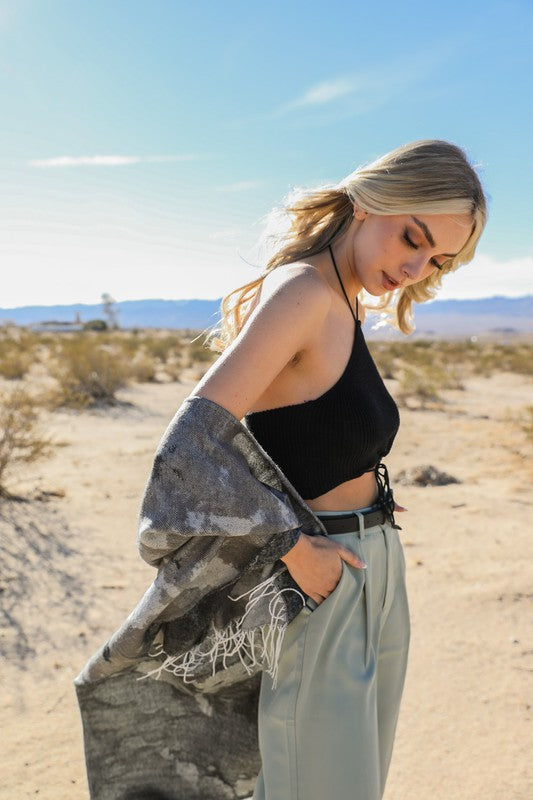 Woman in a desert setting wearing a black top and light pants with a camouflage jacket.