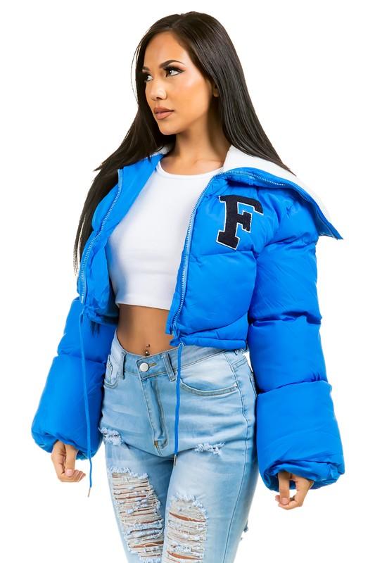 Woman wearing a blue puffer jacket with a white top and ripped jeans on a white background