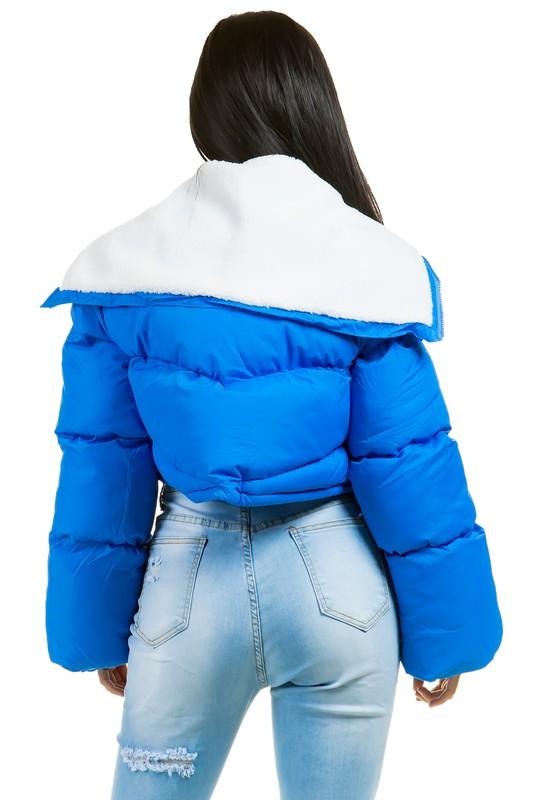 Blue puffer jacket with white hood worn by a person on a white background